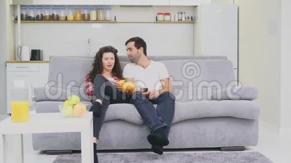 微笑的妻子和男人坐在沙发上在床上吃薯片的时候看电视穿着黑色牛仔裤视频的预览图