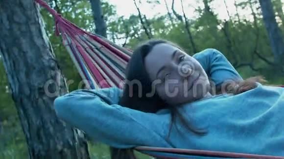 美丽快乐的年轻女子在公园的吊床上微笑在树荫下一个女孩在一个视频的预览图