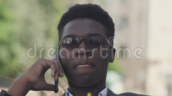 快乐的非洲男人坐在外面用智能手机说话的肖像视频的预览图