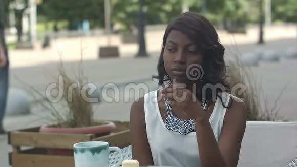 有非洲发型的严肃黑人妇女穿着正式的白色上衣坐在咖啡馆等她的朋友视频的预览图
