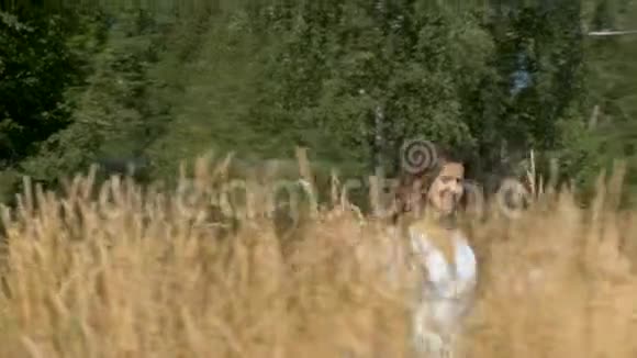 年轻漂亮的女人穿着白色连衣裙带着小麦跑过田野视频的预览图