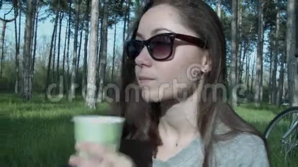 一个戴眼镜的女孩在公园里安排了一顿午餐他喝咖啡在一个美丽的夏天吃东西年轻漂亮视频的预览图
