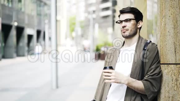 戴眼镜的英俊青年喝着咖啡在街上等着视频的预览图