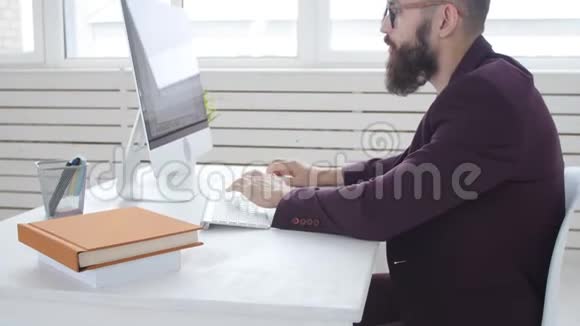 办公室工作或自由职业者的概念年轻的留胡子的时髦男人在办公室的电脑里工作视频的预览图