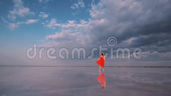 女游客穿着一件挥舞的裙子沿着一个天空反射的盐湖散步视频的预览图