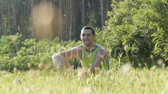 夏天在森林背景下年轻英俊开朗的男人坐在草地上环顾四周视频的预览图