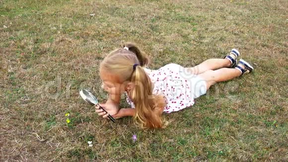 女孩用放大镜躺在草坪上一个女孩透过放大镜漂亮的女孩拿着放大镜视频的预览图