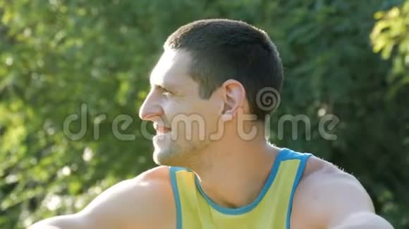 夏天在森林背景下年轻英俊开朗的男人坐在草地上环顾四周视频的预览图