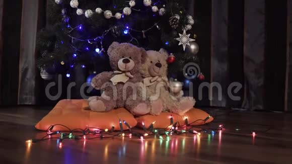 骑在两只玩具泰迪熊上的相机坐在一棵圣诞装饰树附近的橙色枕头上圣诞装饰视频的预览图