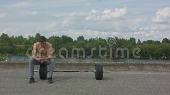 男运动员在户外进行积极的激烈训练后在休息时使用手机视频的预览图