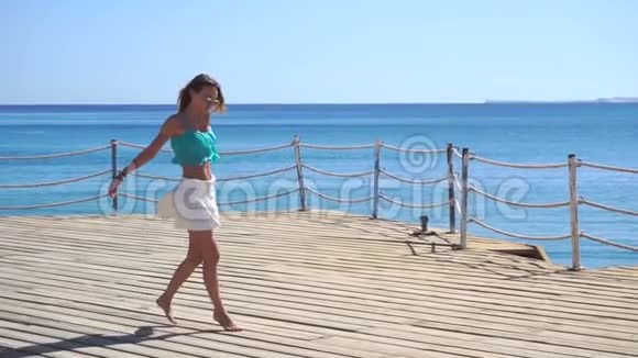 戴着眼镜和裙子的小女孩在海滩上慢跑着视频的预览图
