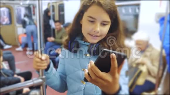 十几岁的女孩带着智能手机和耳机在地铁里很多人挤在地铁里地铁视频的预览图