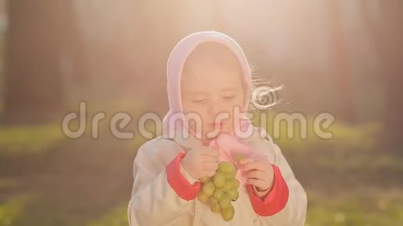 一个穿着粉红色头巾的俄罗斯小女孩在日落时吃葡萄视频的预览图