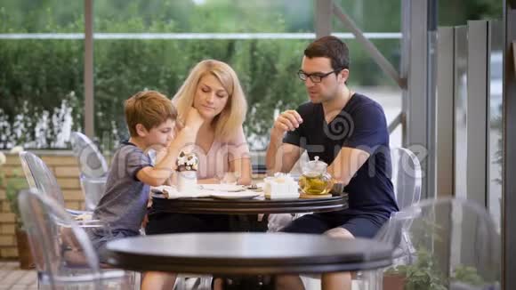 幸福的家庭和儿子一起在户外露台上度过时光妻子和丈夫在男孩吃甜点时聊天视频的预览图