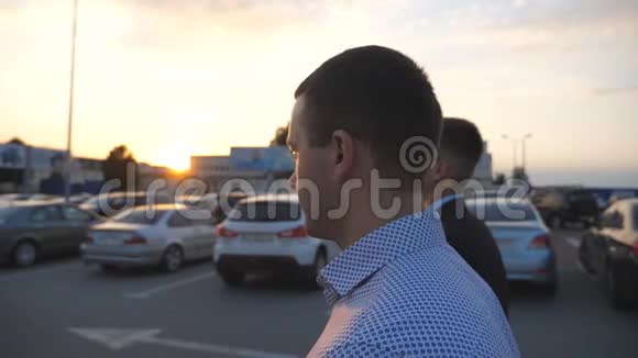 日落时分两个年轻的商人在汽车停车场散步商人们一起上下班自信的人视频的预览图