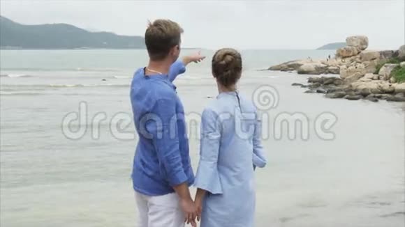 一个人向地平线和大海上的大石头伸出他的手年轻的一对夫妇手牵手在海边视频的预览图