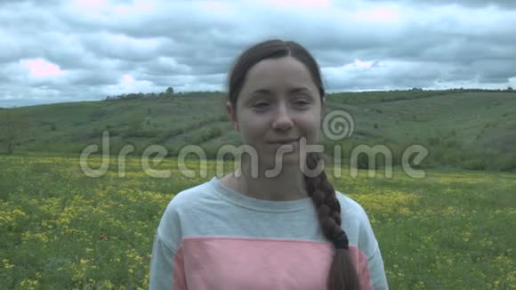 一个美丽的微笑女孩在田野和浓密的云彩的肖像快乐的年轻女子在一片有黄色花朵和视频的预览图