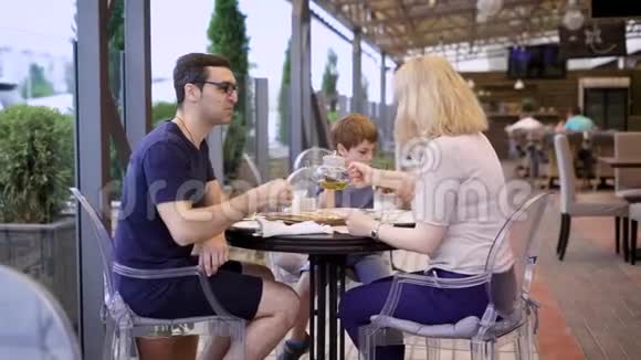 快乐的夫妻和儿子一起在户外露台上坐在桌子旁妻子和丈夫在男孩时交谈视频的预览图