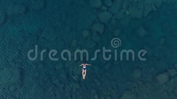 空中慢动作女人漂浮在蓝色水面上在透明的地中海游泳俯视夏季度假视频的预览图