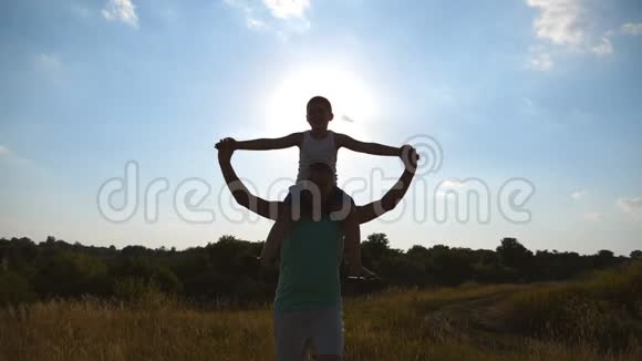 小男孩坐在他爸爸的肩膀上在日落时举起手作为飞机父子幸福视频的预览图