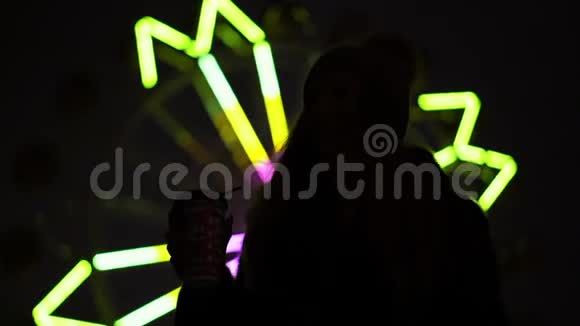 摩天轮闪烁的灯光背景下一个拿着N咖啡的女孩的剪影视频的预览图