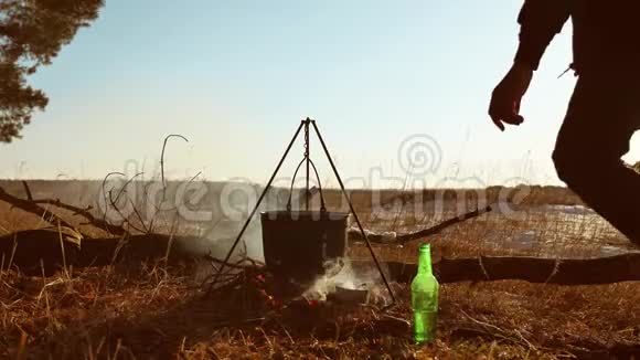 一个人坐在火边在一个露营地停下来一个人在水壶里的水沸腾阳光直射着他视频的预览图