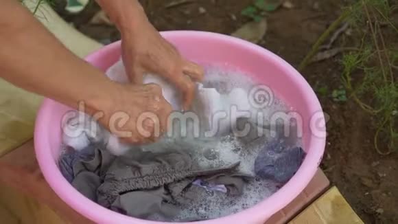 老妇人用粉红色塑料碗洗衣服视频的预览图