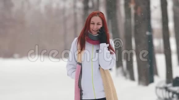 冬季公园一位笑容可掬的红发女人在电话里交谈视频的预览图