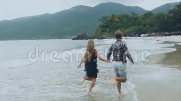 恋爱中的年轻夫妇牵着手在海边奔跑慢动作地笑着幸福的概念视频的预览图