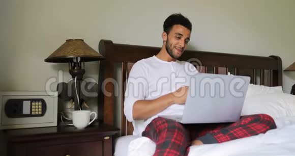 使用笔记本电脑坐在床上的思考者西班牙裔在床上聊天的人视频的预览图