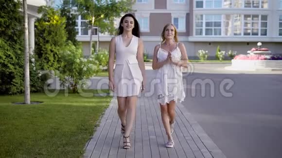 两个穿着白色连衣裙的漂亮女人走在小巷里谈论着生活和事件视频的预览图