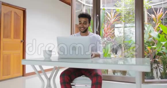 年轻男子在家中使用笔记本电脑坐桌西班牙裔男子打字视频的预览图