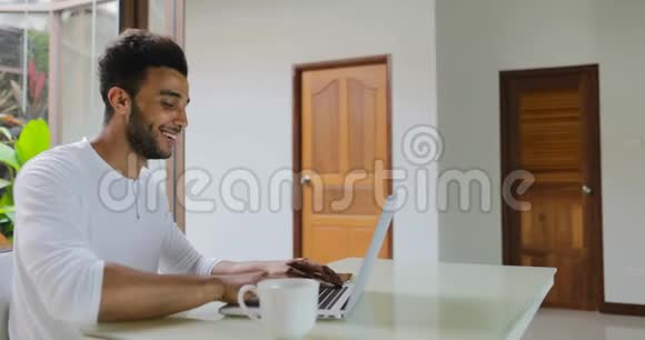 年轻男子在家中使用笔记本电脑坐桌西班牙裔男子打字视频的预览图