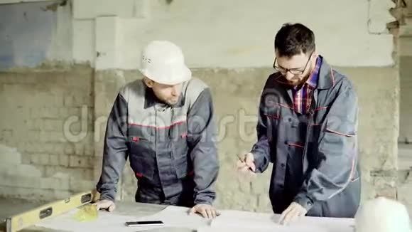戴着防护头盔的工程师和工头在施工图中做笔记这些人在一家工厂里视频的预览图