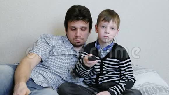 在沙发上看电视无聊的男孩和他爸爸正在看电视并切换频道视频的预览图