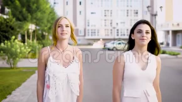 两个穿着白色连衣裙的漂亮女人走在小巷里谈论着生活和事件视频的预览图