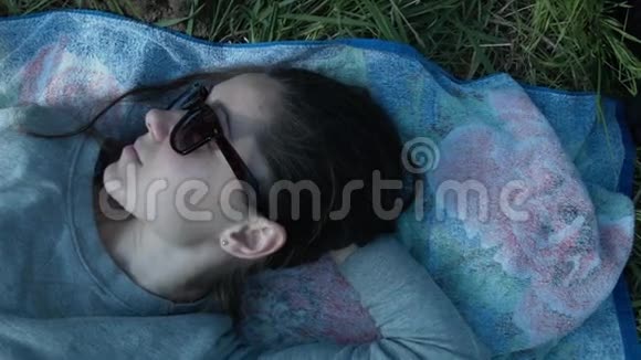 戴眼镜的女孩躺在绿草中的垃圾上美丽的年轻女子躺在田野上视频的预览图