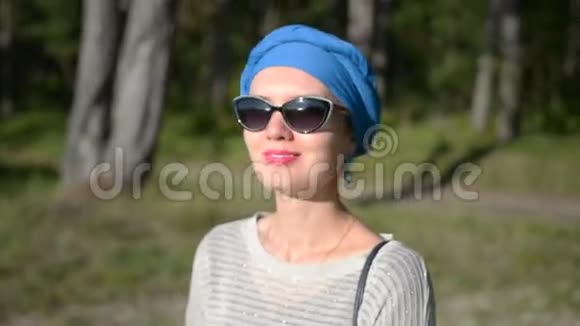 幸福的女人站在海滩附近的森林里戴着头巾和太阳镜向前看微笑着视频的预览图