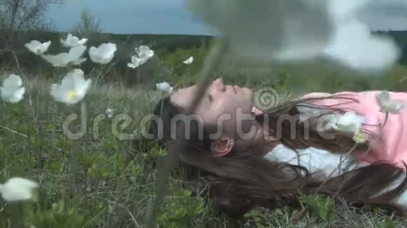 可爱的女孩躺在白花绿的草地上一个年轻的女人正在依靠大自然一片花草甸上的美景视频的预览图