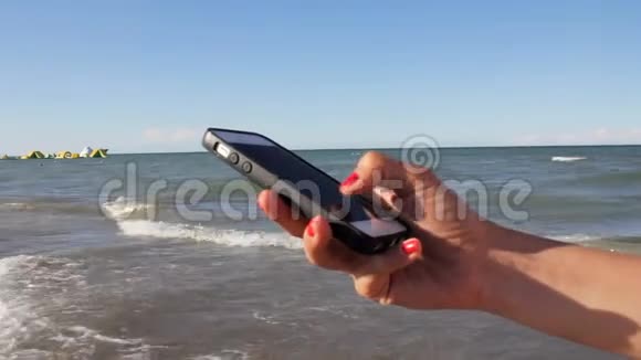 穿比基尼的女人在海滩上用智能手机发短信户外使用智能手机特写双手移动视频的预览图