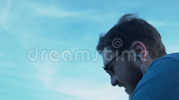 一个微笑的年轻人带着耳机和眼镜看着飞机上的天空一位英俊的年轻人的肖像视频的预览图
