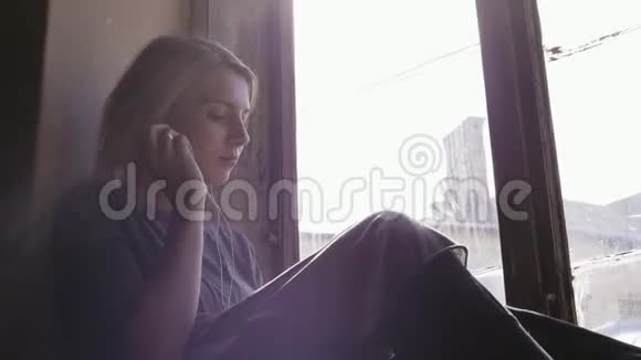 女孩看起来很伤心一边在窗边的耳机上听音乐特写视频的预览图