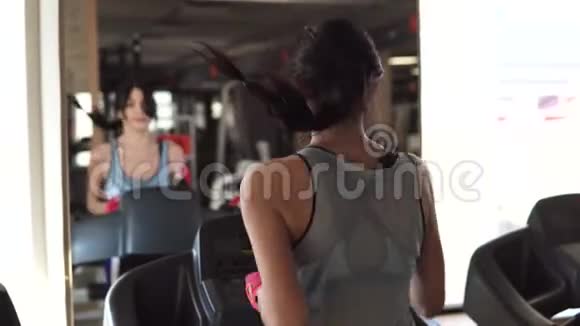 年轻女子在健身房的跑步机上跑步后面的景色视频的预览图