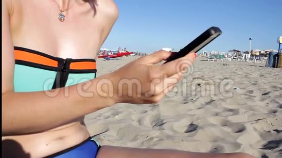 穿比基尼的女人在海滩上用智能手机发短信户外使用智能手机特写双手移动视频的预览图