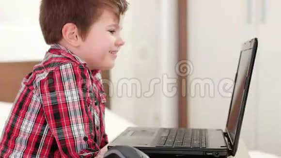 快乐的孩子通过笔记本电脑天空微笑的孩子在家小男孩看有趣的卡通在小玩意视频的预览图