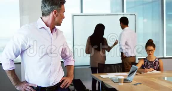 当同事在后台工作时行政人员双手叉腰站立的肖像视频的预览图
