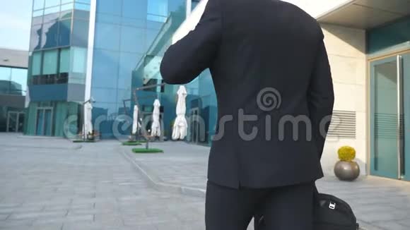 跟随年轻的商人带着公文包走在现代办公楼附近戴太阳镜上下班的商人视频的预览图