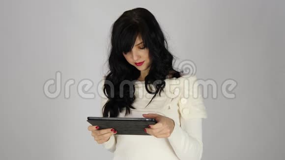 一个笑的女人用平板电脑在灰色背景下孤立地看着相机和微笑的肖像视频的预览图