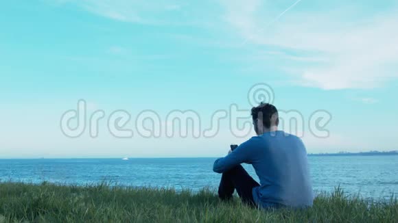 一个年轻人坐在海边的草地上写短信船在经过飞机在空中飞行视频的预览图