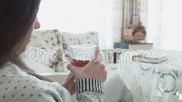 一个甜美的年轻女人正在喝茶穿着睡衣看书一位美丽的年轻女子正在喝茶吃东西视频的预览图
